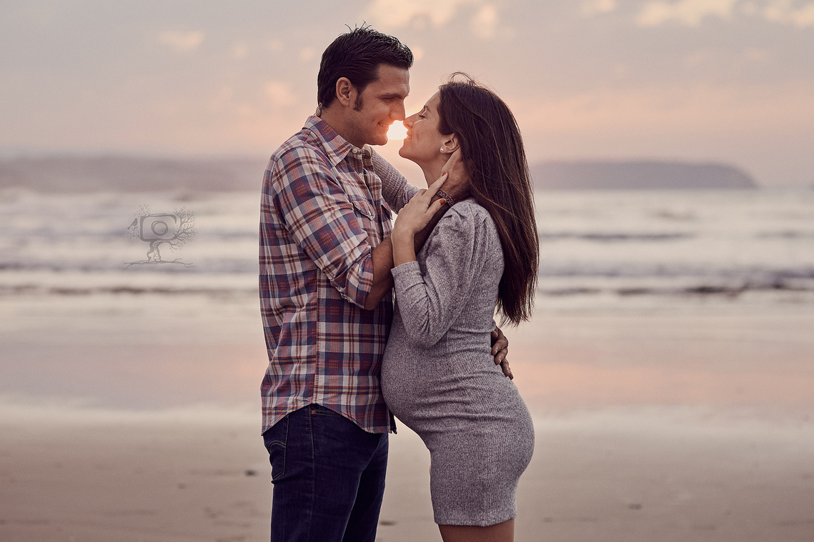Mujer embarazada con su pareja al atardecer en la playa