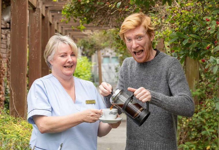 Press PR Photocall image of Irish actor Domhnall Gleeson pouring a coffee for a Hospice nurse. To support Bewleys big coffee morning social for hospice. Professional PR photographer Dublin www.1image.ie