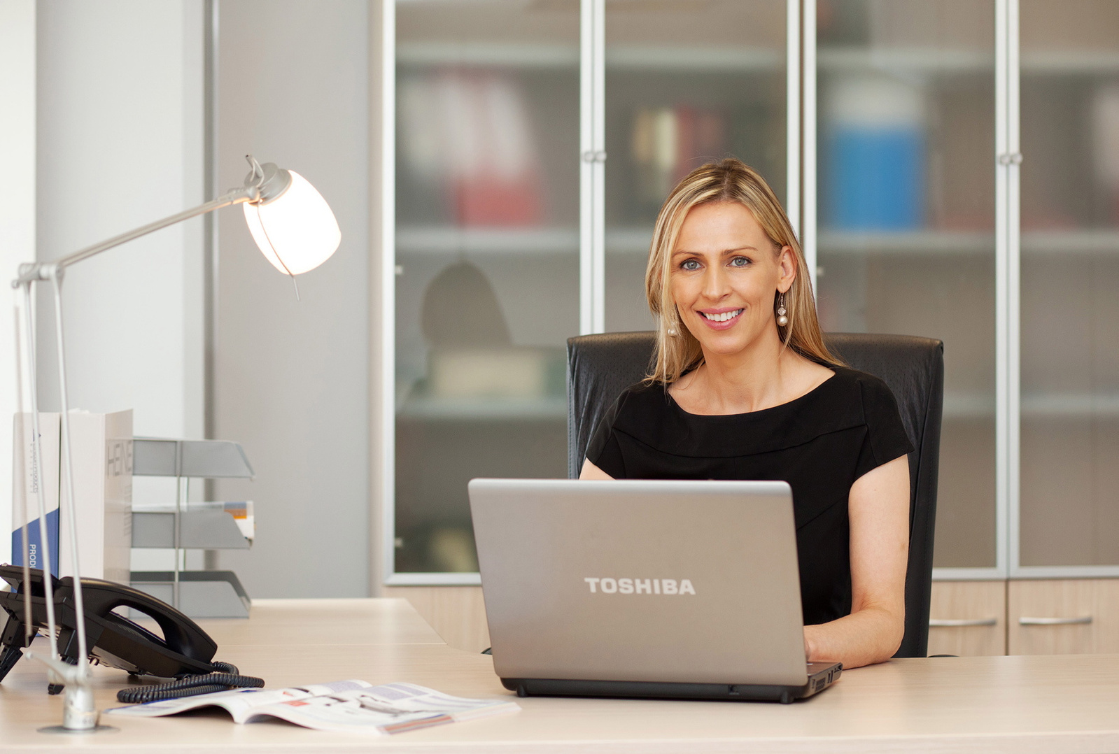 Corporate business portrait photography. Businesswoman in office environment working at laptop professional portrait for website