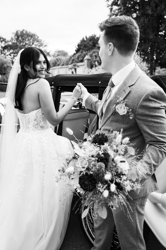 Groom helping his bride get into a vintage car at a wedding at Guildford Manor Hotel and Spa