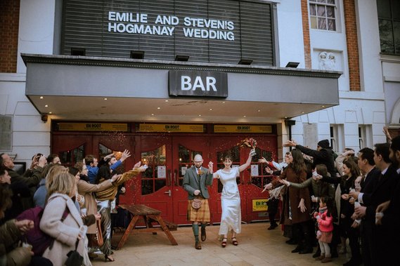 A candid shot of the bride and groom laughing together during their wedding confetti toss in South London at their chosen venue, the Ritzy Cinema in Brixton