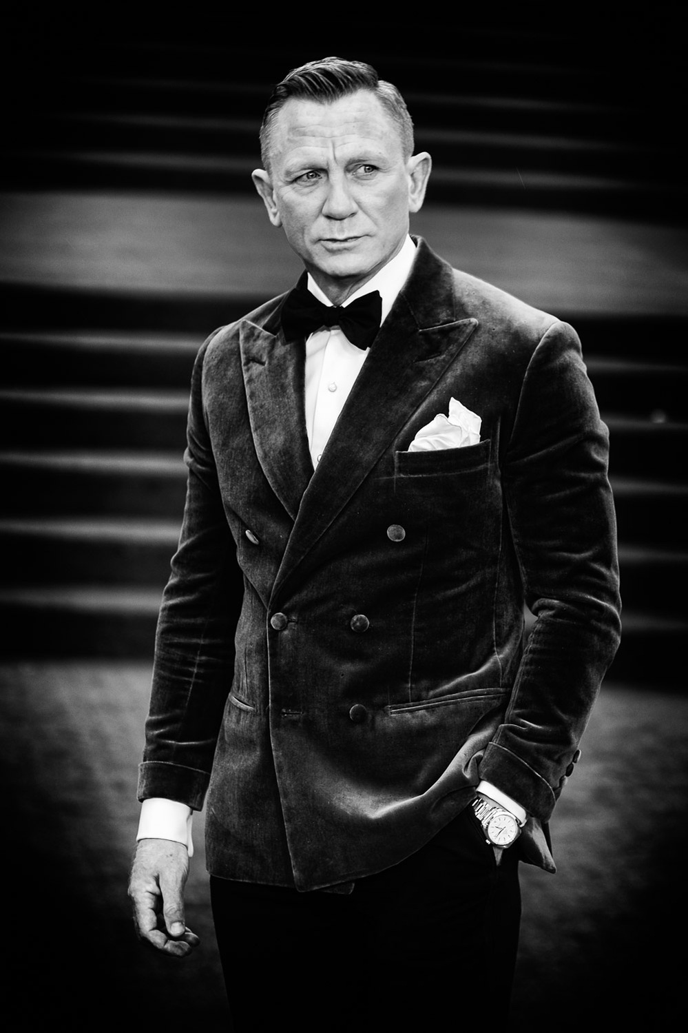 Black and white image of Danial Craig in black tie, hand in pocket.