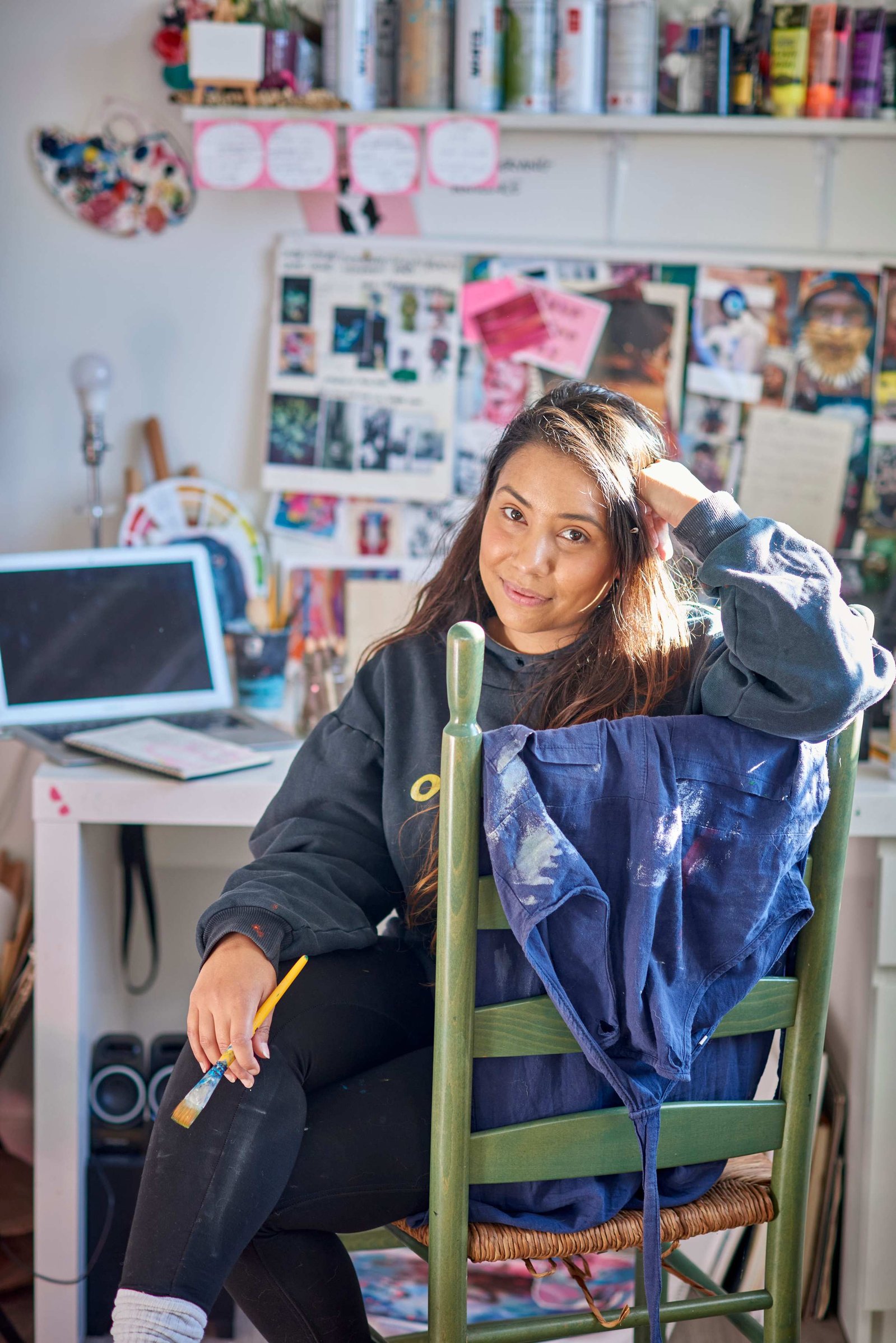woman sitting on green chair with paintbrush in hand.