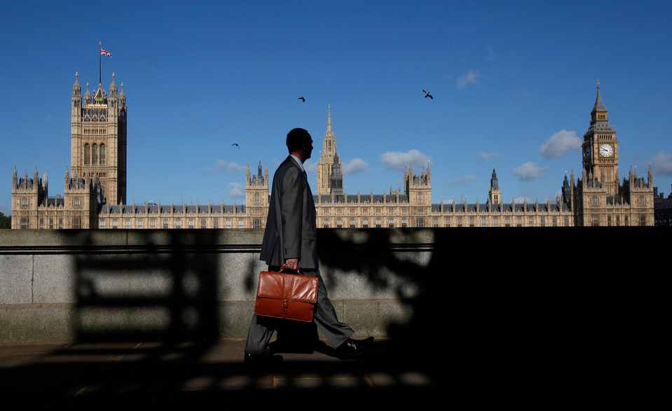 a man with a briefcase walking past the houses of parliament 