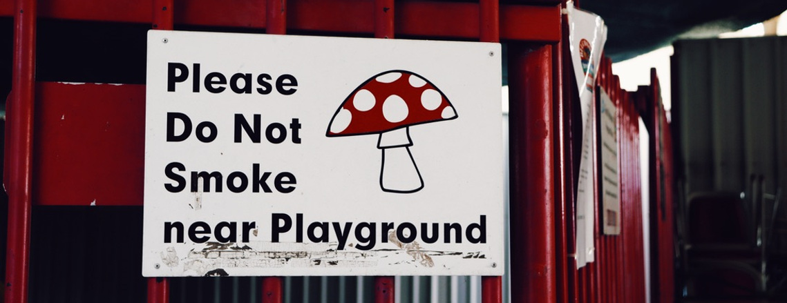 A sign on a fence that features an illustration of a cartoon mushroom and reads: Please do not smoke near playground. 
