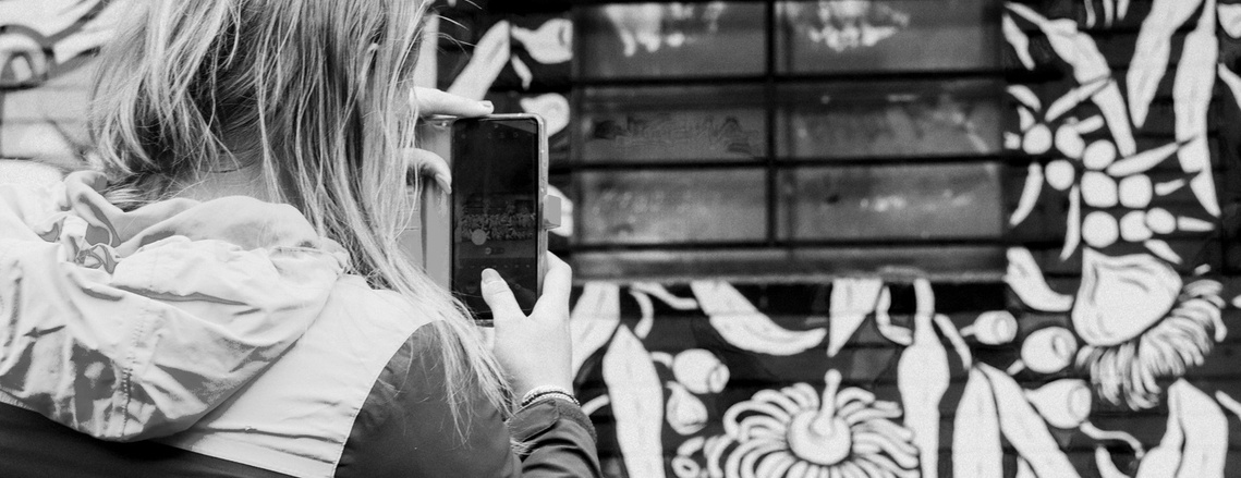 A passerby takes a photo of a mural with their phone.