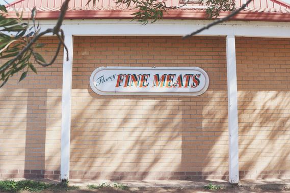 A brick wall dappled in sunlight with a sign that reads: Florey Fine Meats