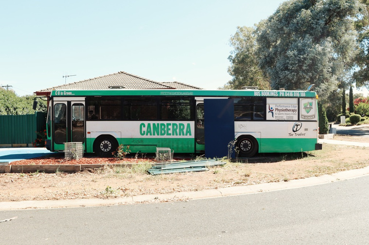 An old Canberra bus parked in someone's front yard. 
