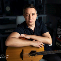 Portrait of a musician seated in a recording studio, resting on an acoustic guitar, surrounded by audio equipment. Perfect for music production branding, artist profiles, or creative promotions.