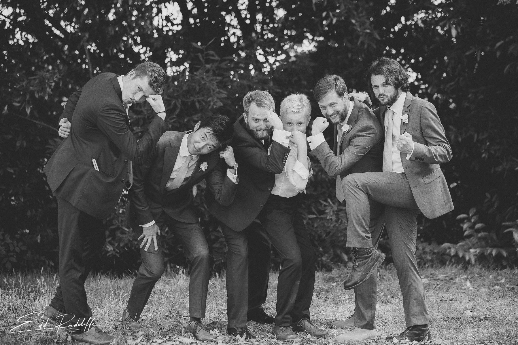 Groom and Groomsmen strike strongman poses in front of trees at Hôtel de Cours de Thomazeau in Castilliones for Edd Radcliffe Photography - documentary style wedding photography