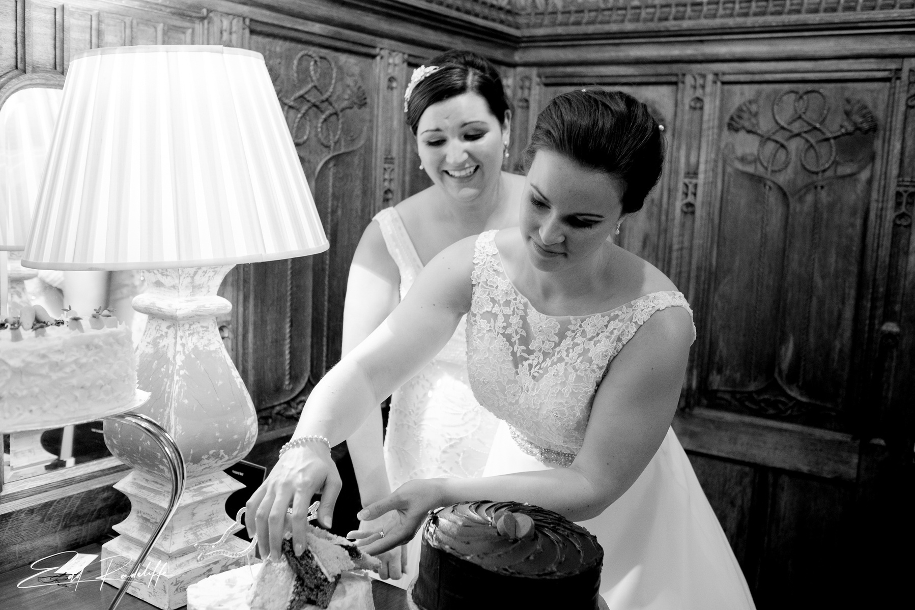 Bride helps herself to slice of wedding cake while Bride stands behind laughing at Carlton Towers, Yorkshire for Edd Radcliffe Photography - documentary style wedding photography