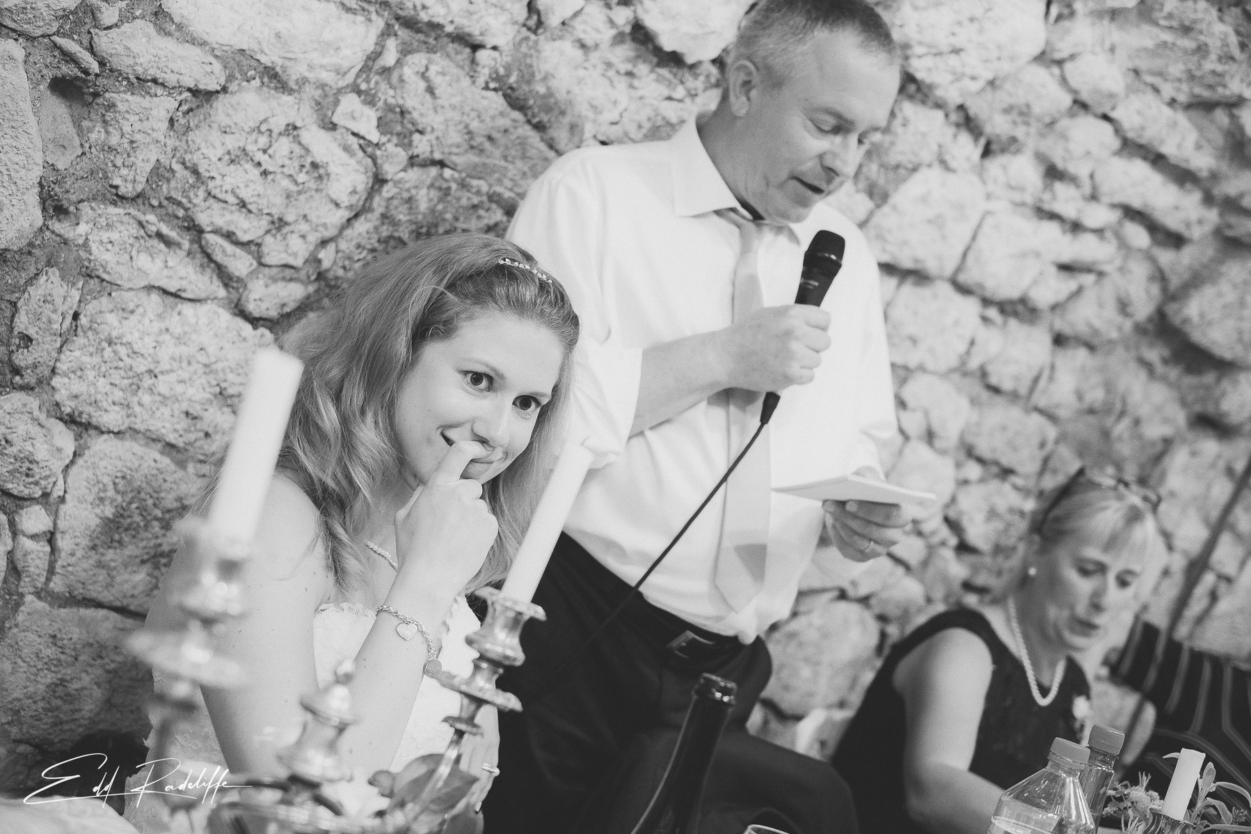 Bride smiles as man gives speech at wedding breakfast at Hôtel de Cours de Thomazeau in Castilliones for Edd Radcliffe Photography - documentary style wedding photography