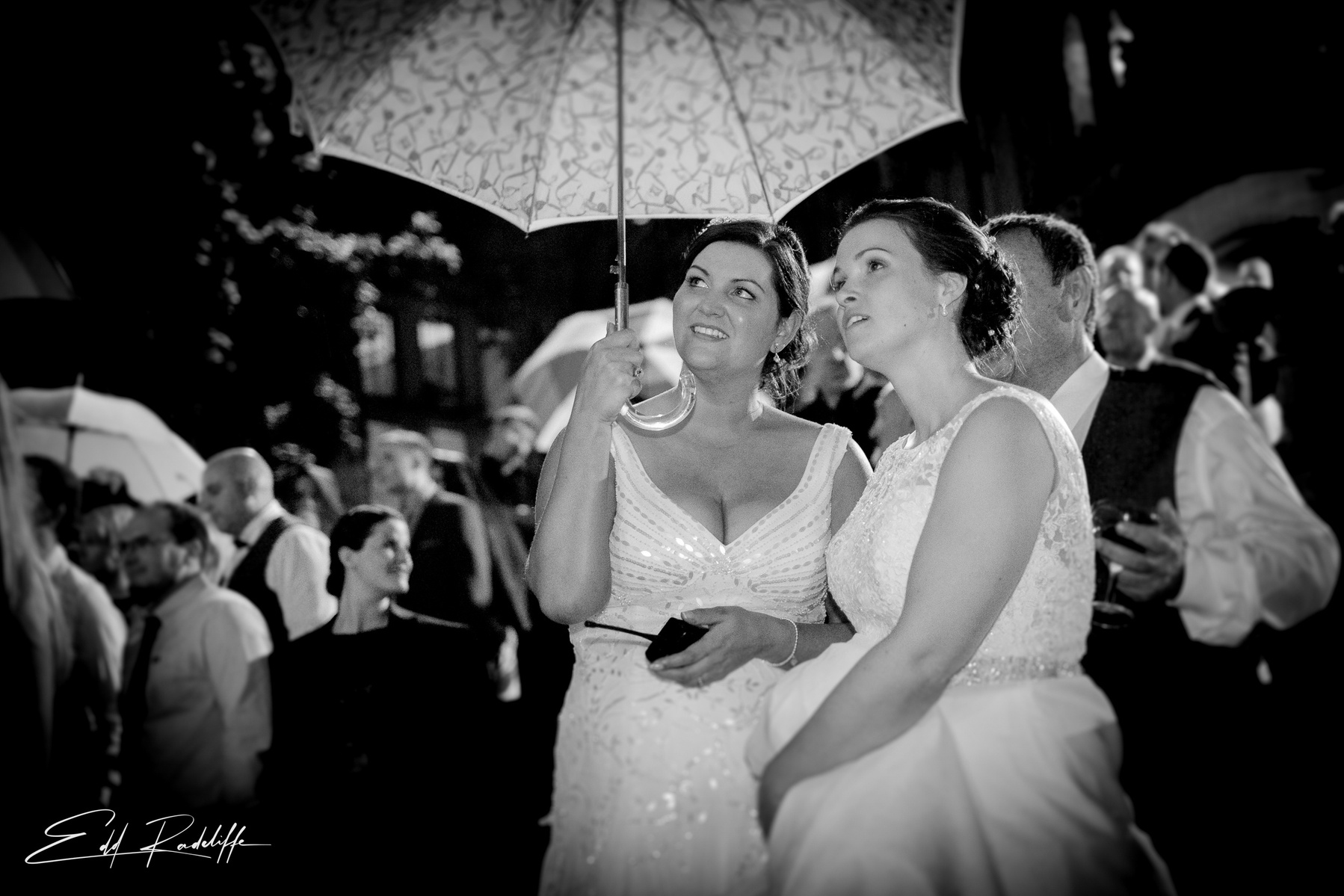 Brides stand together under an umbrella at Carlton Towers, Yorkshire for Edd Radcliffe Photography - documentary style wedding photography