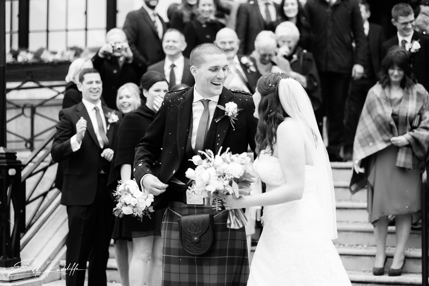 Bride and Groom smile at each other while congregation stands behind them on steps of Islington Town Hall, London for Edd Radcliffe Photography - documentary style wedding photography