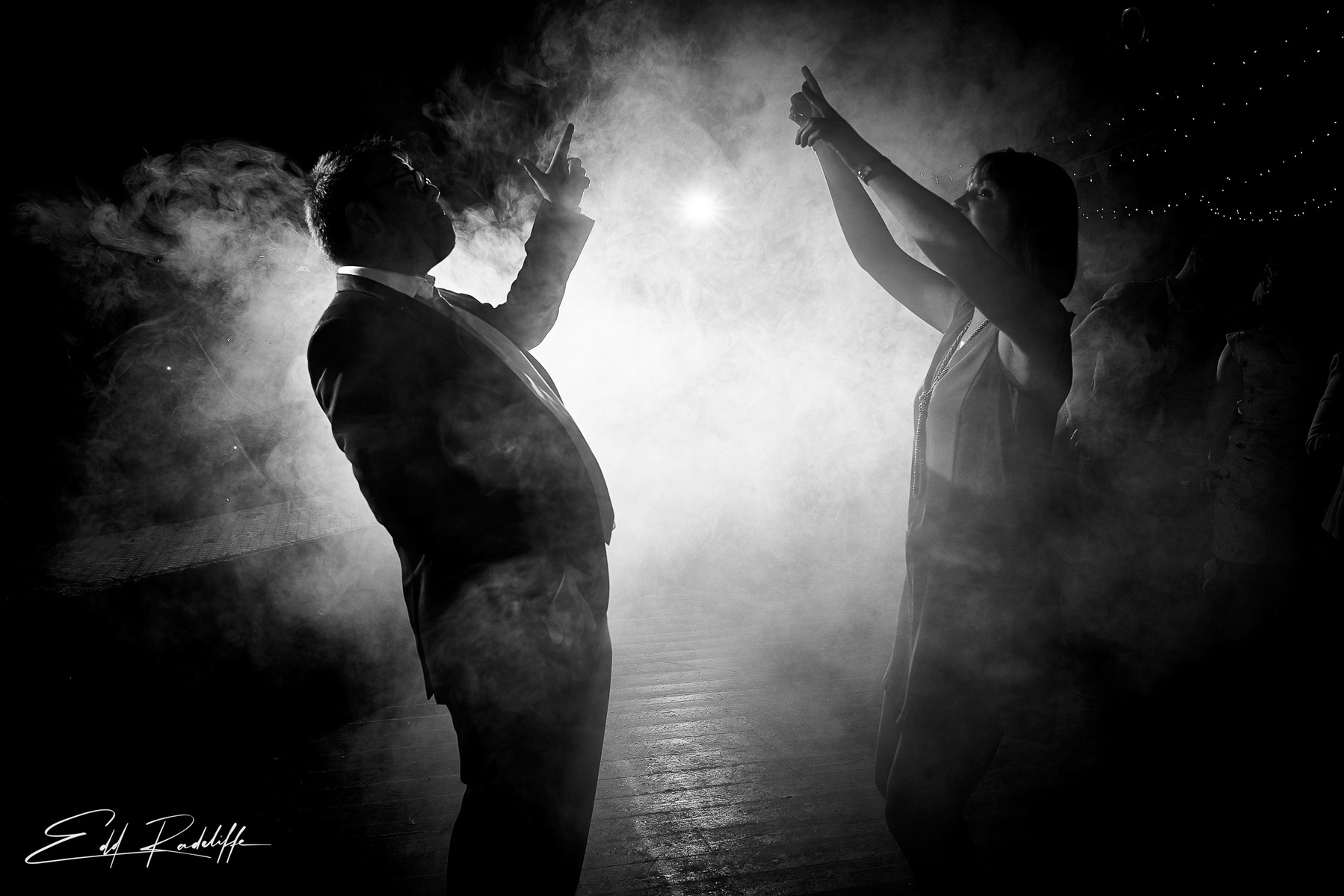 Silhouette of wedding guests dancing with smoky illuminated background at the Square and Compass in Somerset for Edd Radcliffe Photography - documentary style wedding photography