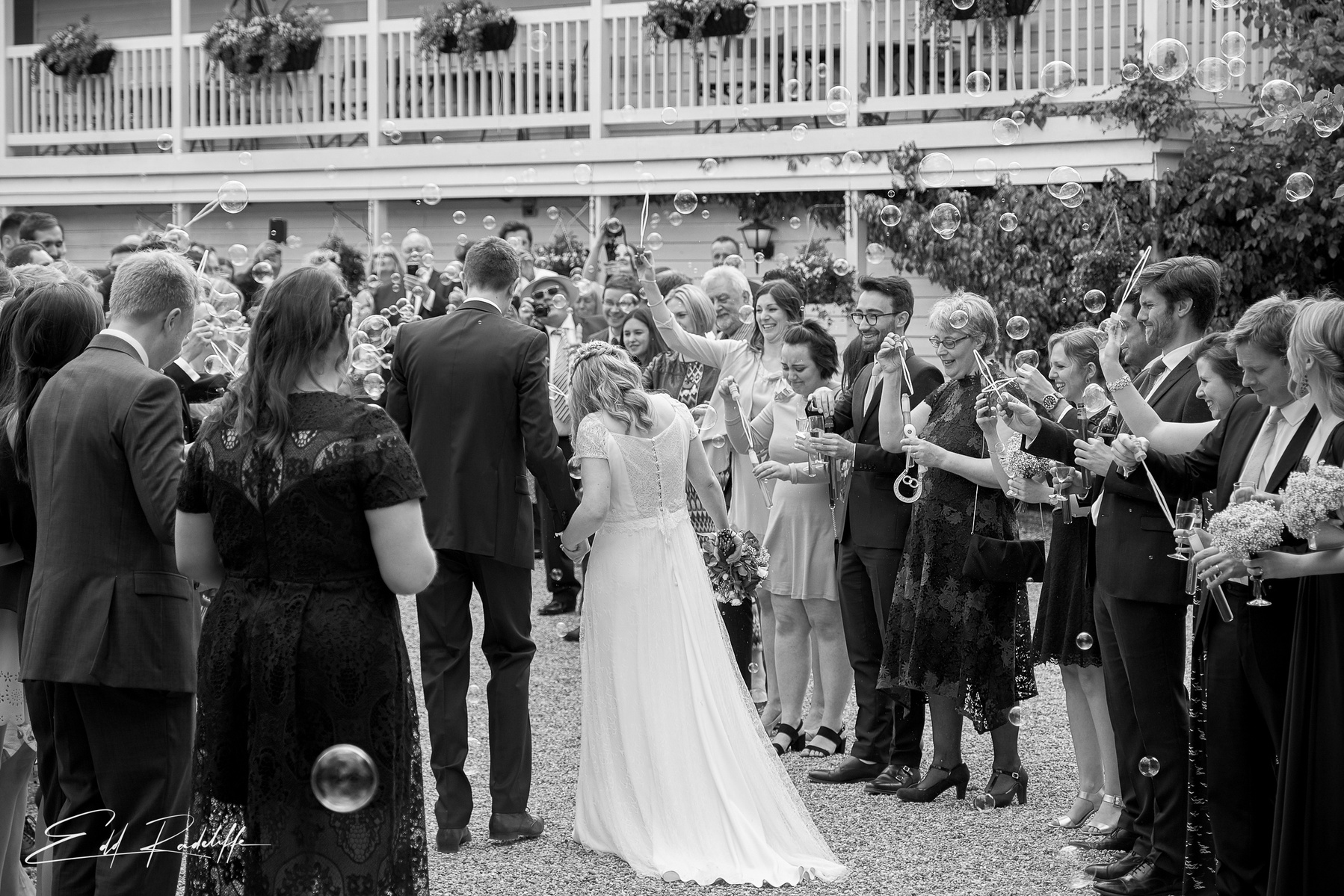 Bride and Groom walk away through congregation as wedding guests blow bubbles at the Reid Rooms, Chelmsford for Edd Radcliffe Photography - documentary style wedding photography