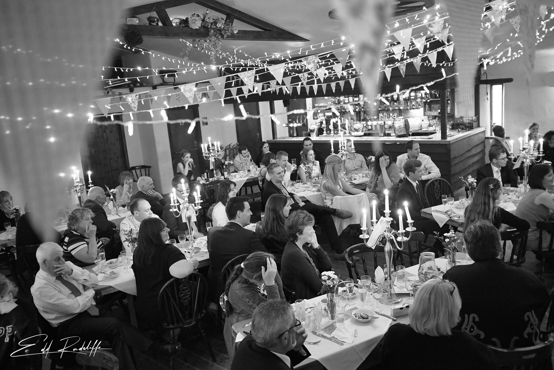 Beautiful view of guests at wedding breakfast, sitting at long tables with bunting overhead. At the Square and Compass in Somerset for Edd Radcliffe Photography - documentary style wedding photography