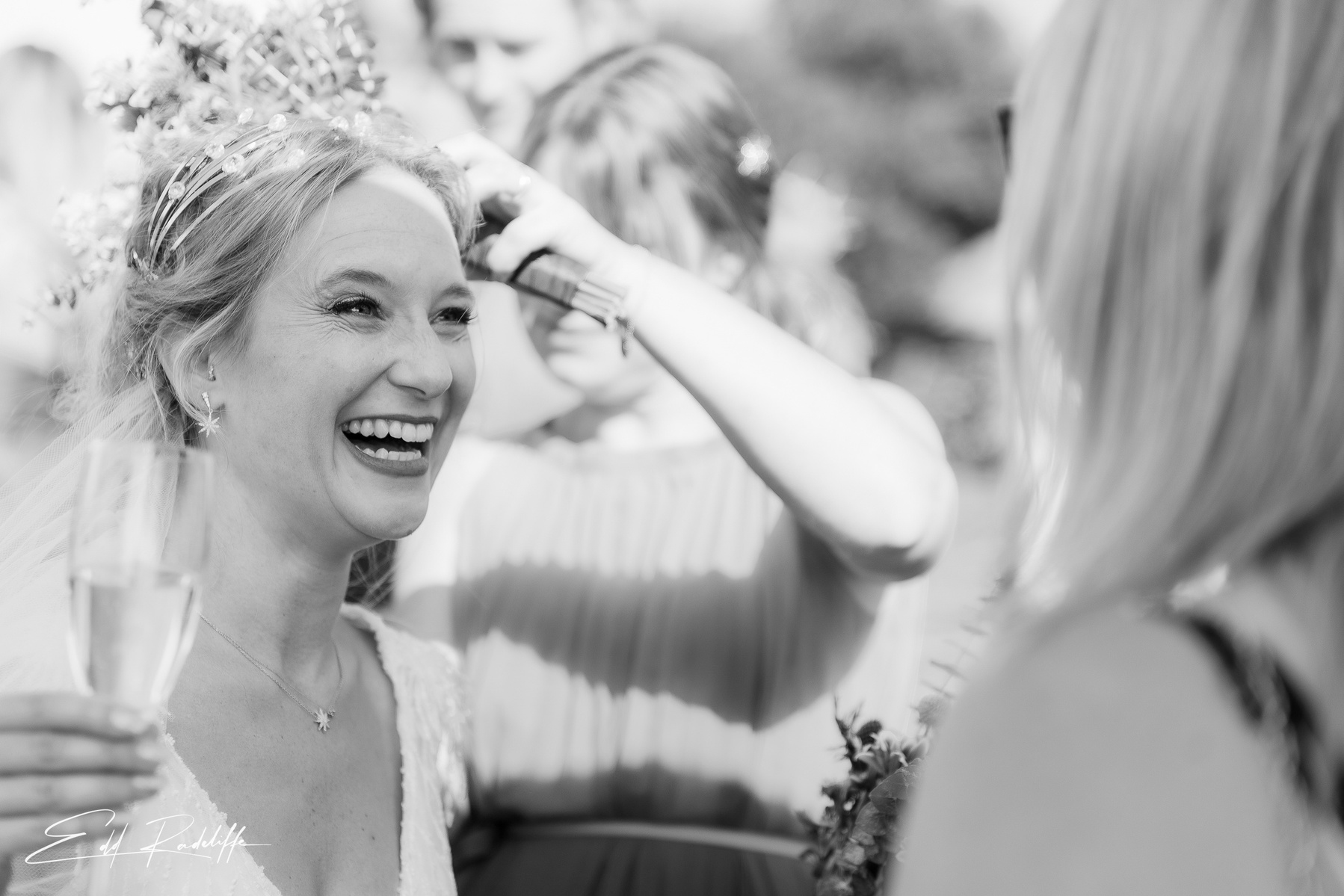 Bride smiles at friend while holding glass of champagne at Groomes in Hampshire for Edd Radcliffe Photography - documentary style wedding photography