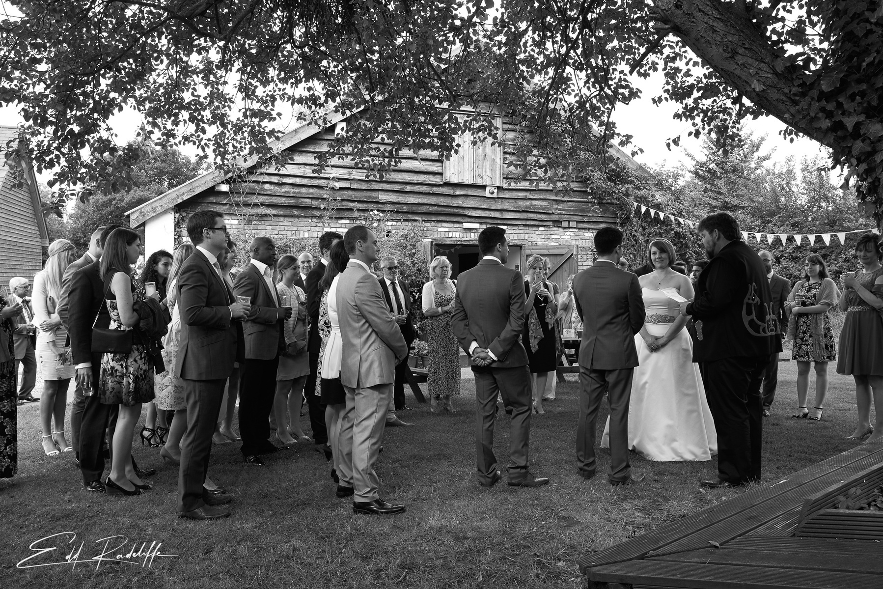 Bride and Groom during ceremony, getting married outside a rustic barn surrounded by congregation at the Square and Compass in Somerset for Edd Radcliffe Photography - documentary style wedding photography