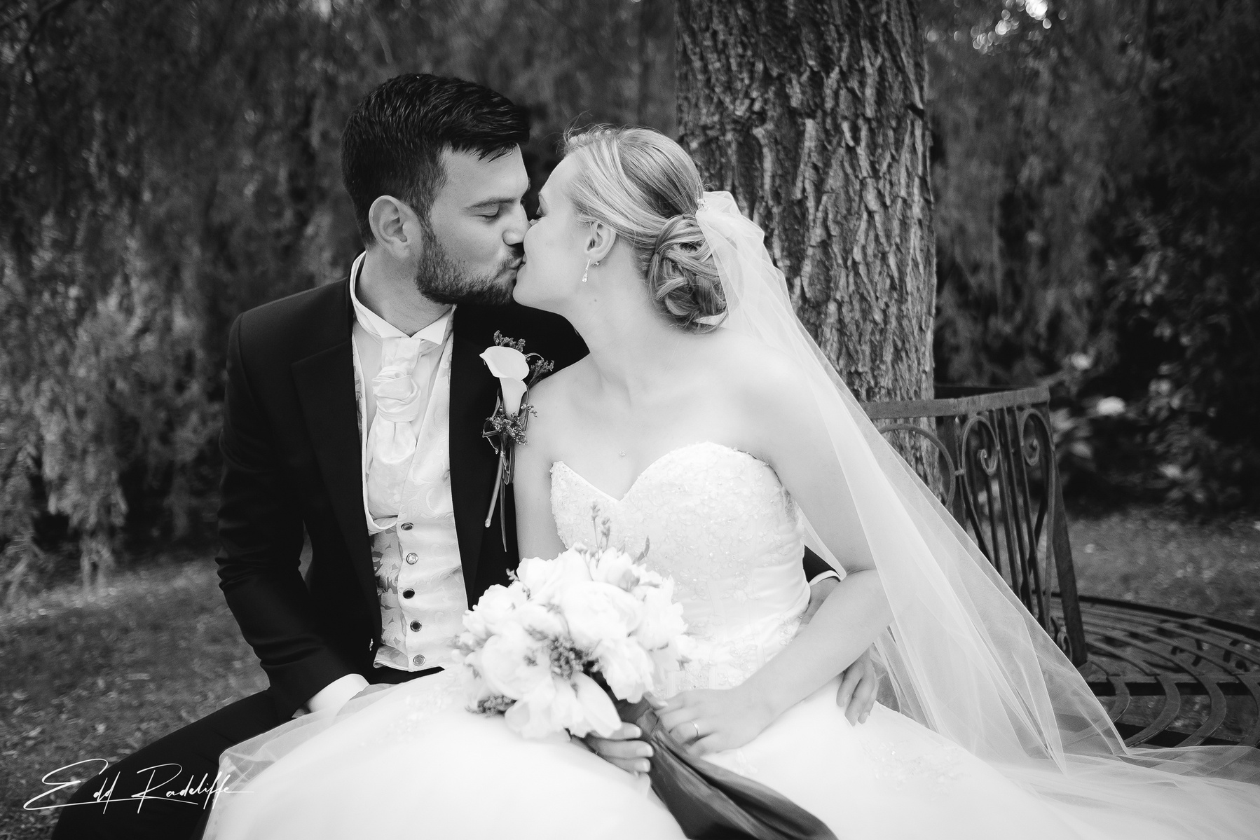 Bride and Groom sit on a bench and kiss at Garons, France for Edd Radcliffe Photography - documentary style wedding photography