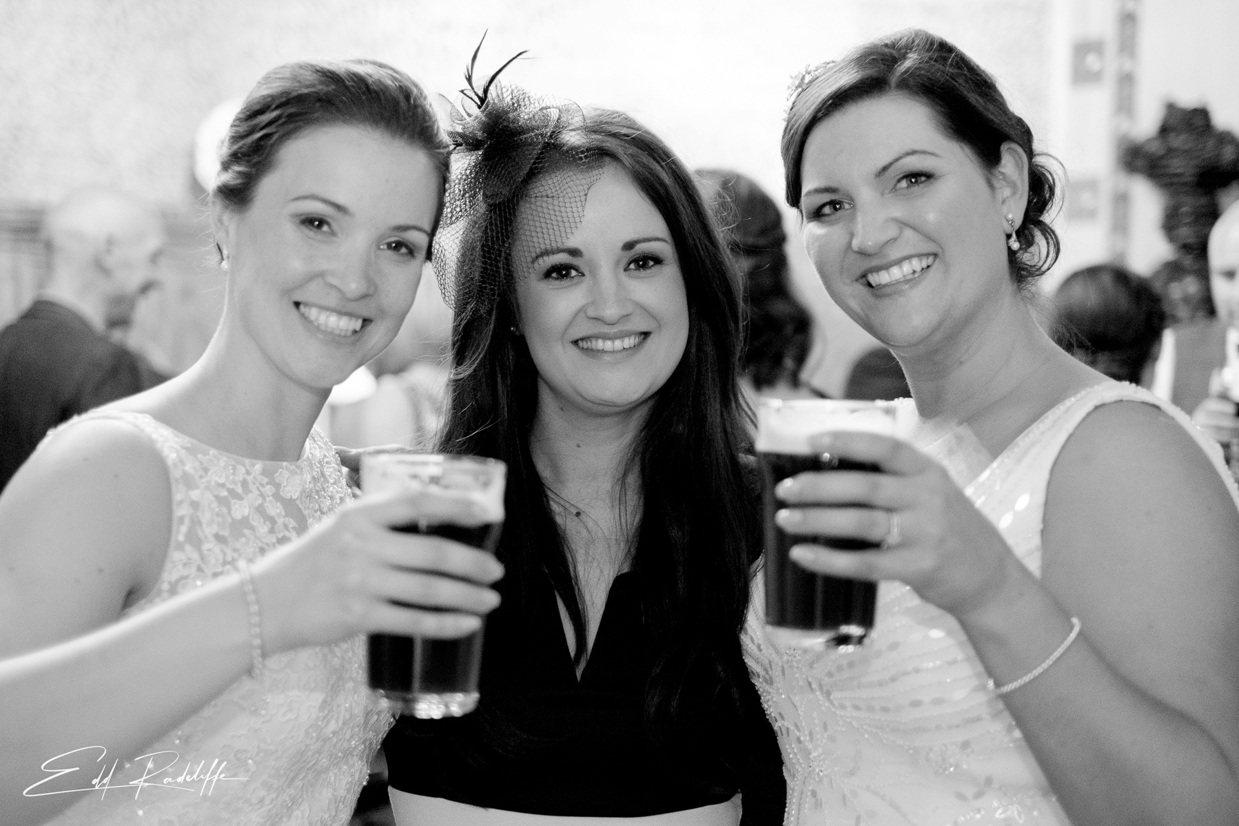 Brides hold up pints while standing on either side of wedding guest at Carlton Towers, Yorkshire for Edd Radcliffe Photography - documentary style wedding photography