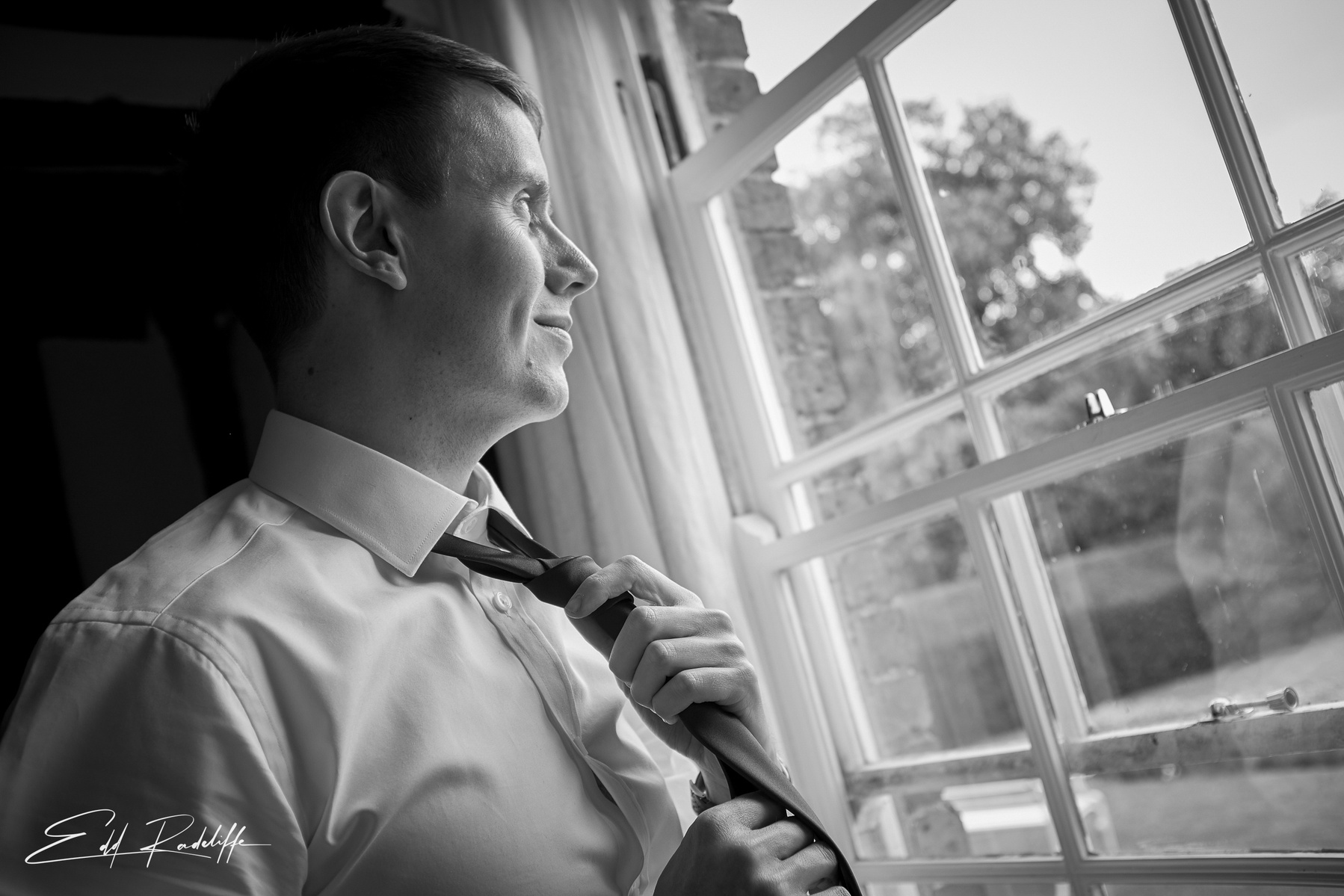 Groom fixes his tie while gazing out of the window at the Reid Rooms, Chelmsford for Edd Radcliffe Photography - documentary style wedding photography