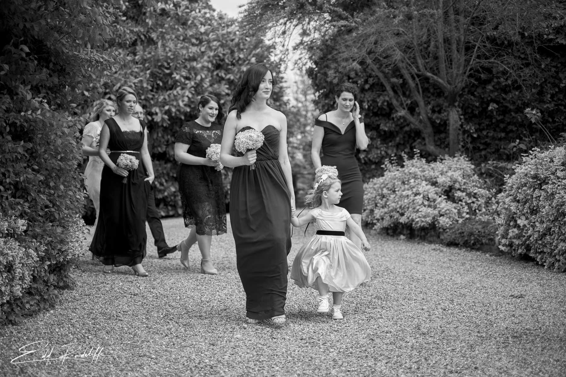  Bridesmaids and flower girl walk down gravel path to ceremony at the Reid Rooms, Chelmsford for Edd Radcliffe Photography - documentary style wedding photography