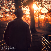 Silhouette of a man in a coat and hat walking through a wooded path at sunset, with warm golden light filtering through trees. Ideal for storytelling, autumn themes, or contemplative branding.