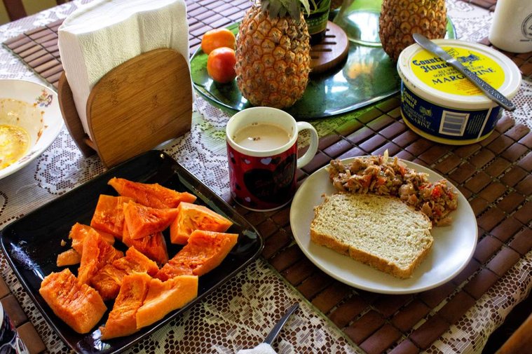 Caribbean breakfast buffet - pineapple, hot tea, papaya, bread and cooked fish on a plate on a tablemat.