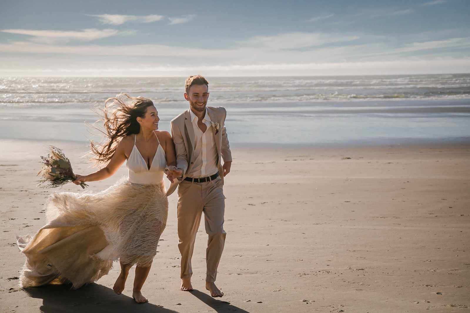 Couple run cheerfully along the Oregon Coast after eloping.