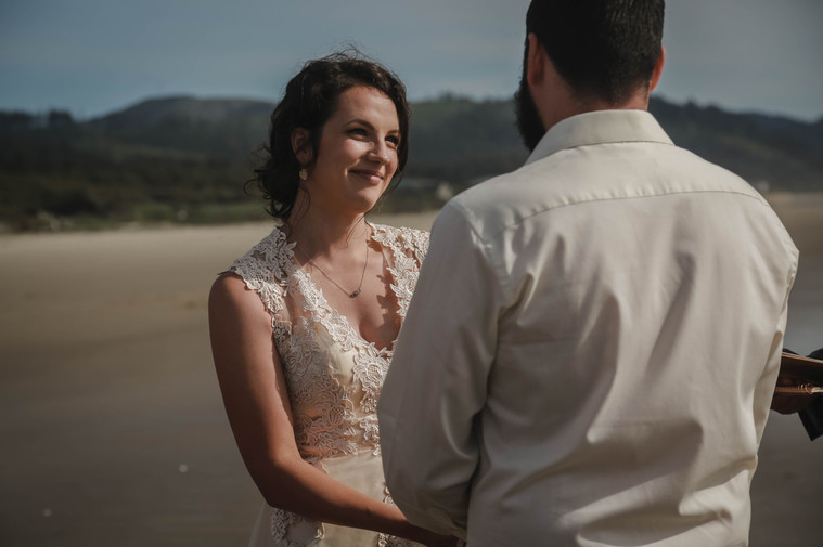 Bride smiles at Groom as they elope near the ocean. The ceremony takes place at Hobbit Beach in Oregon.