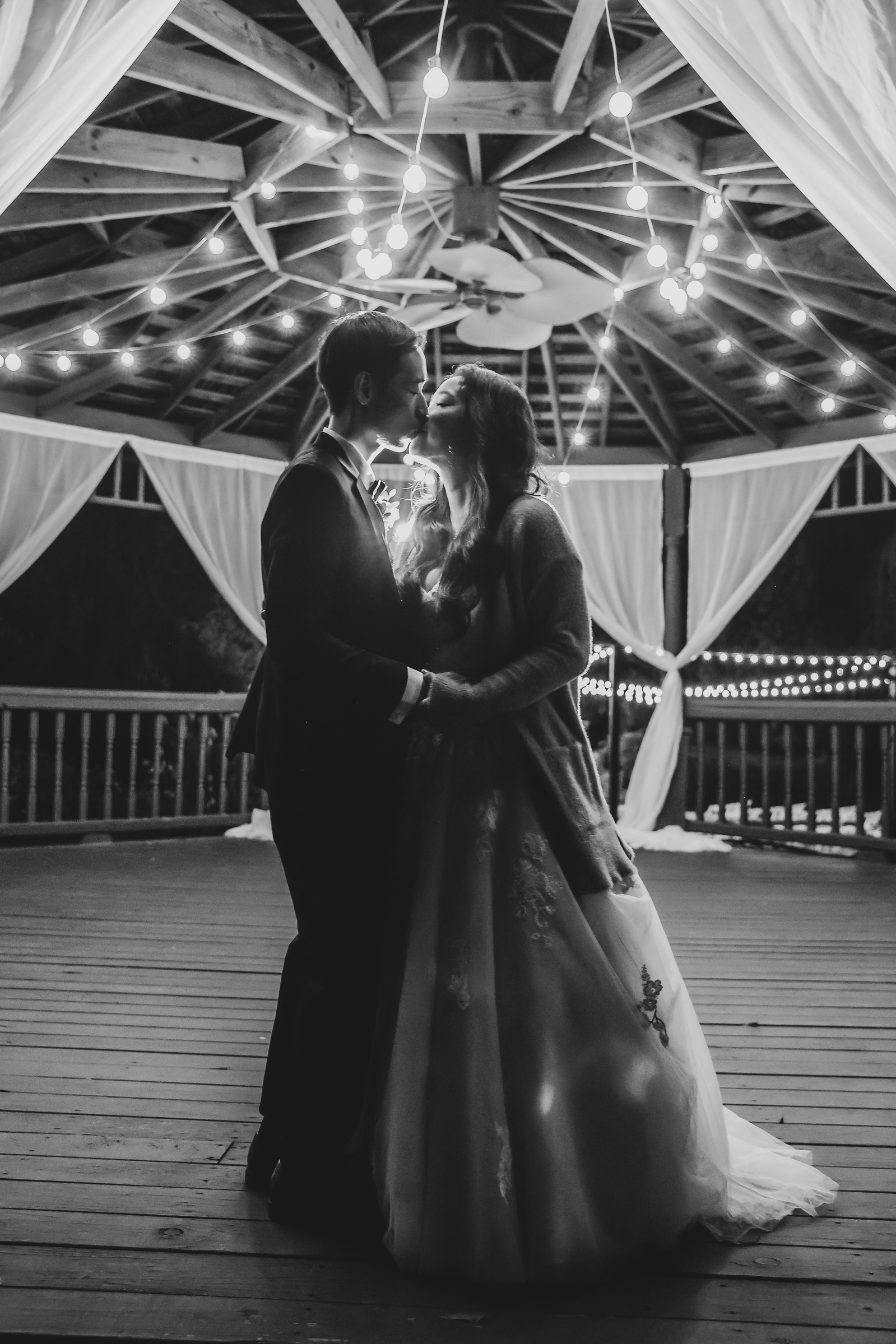black and white image of a bride and groom sharing a last dance in a gazebo surrounded by twinkling lights