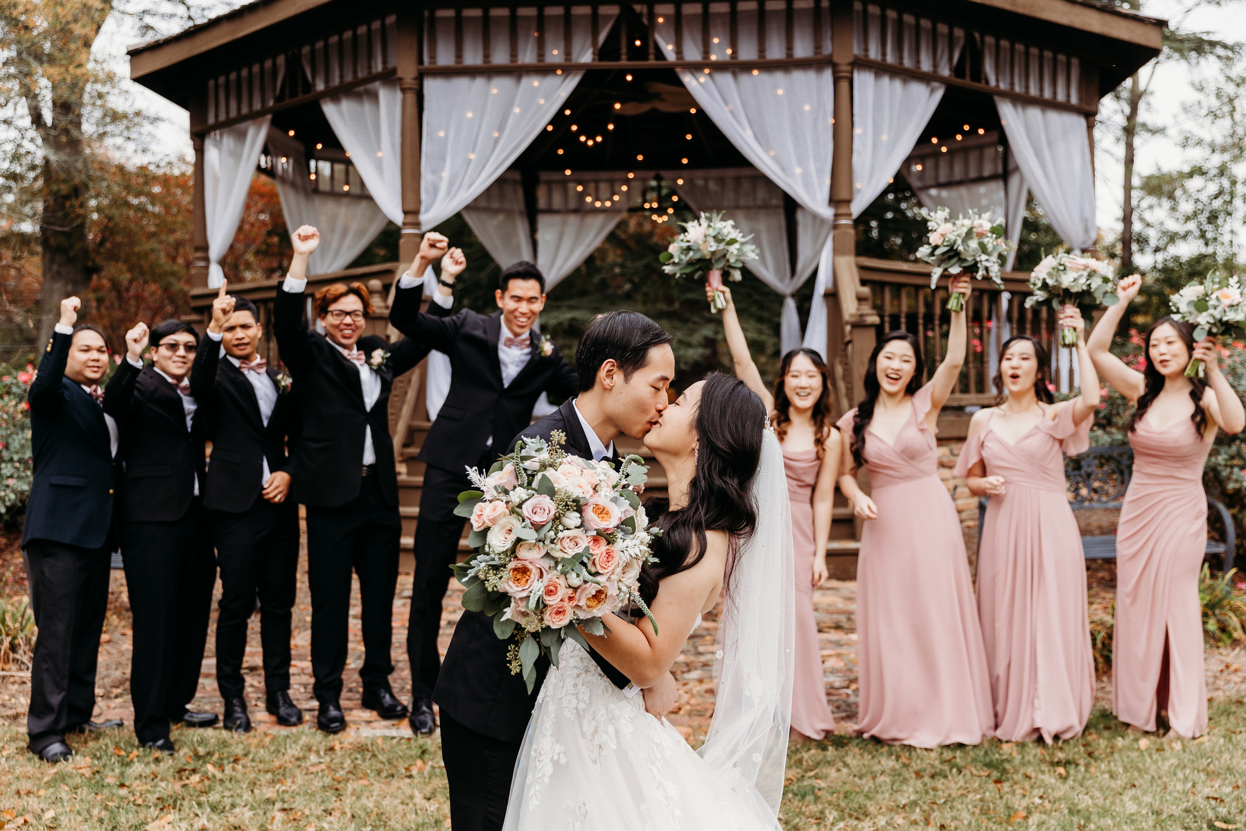 wedding couples kisses as the wedding party cheers them on from behind