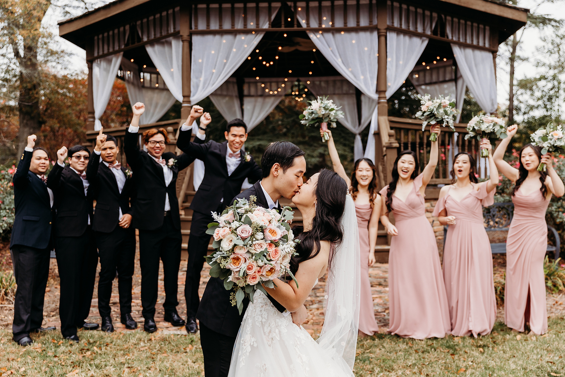 wedding couples kisses as the wedding party cheers them on from behind