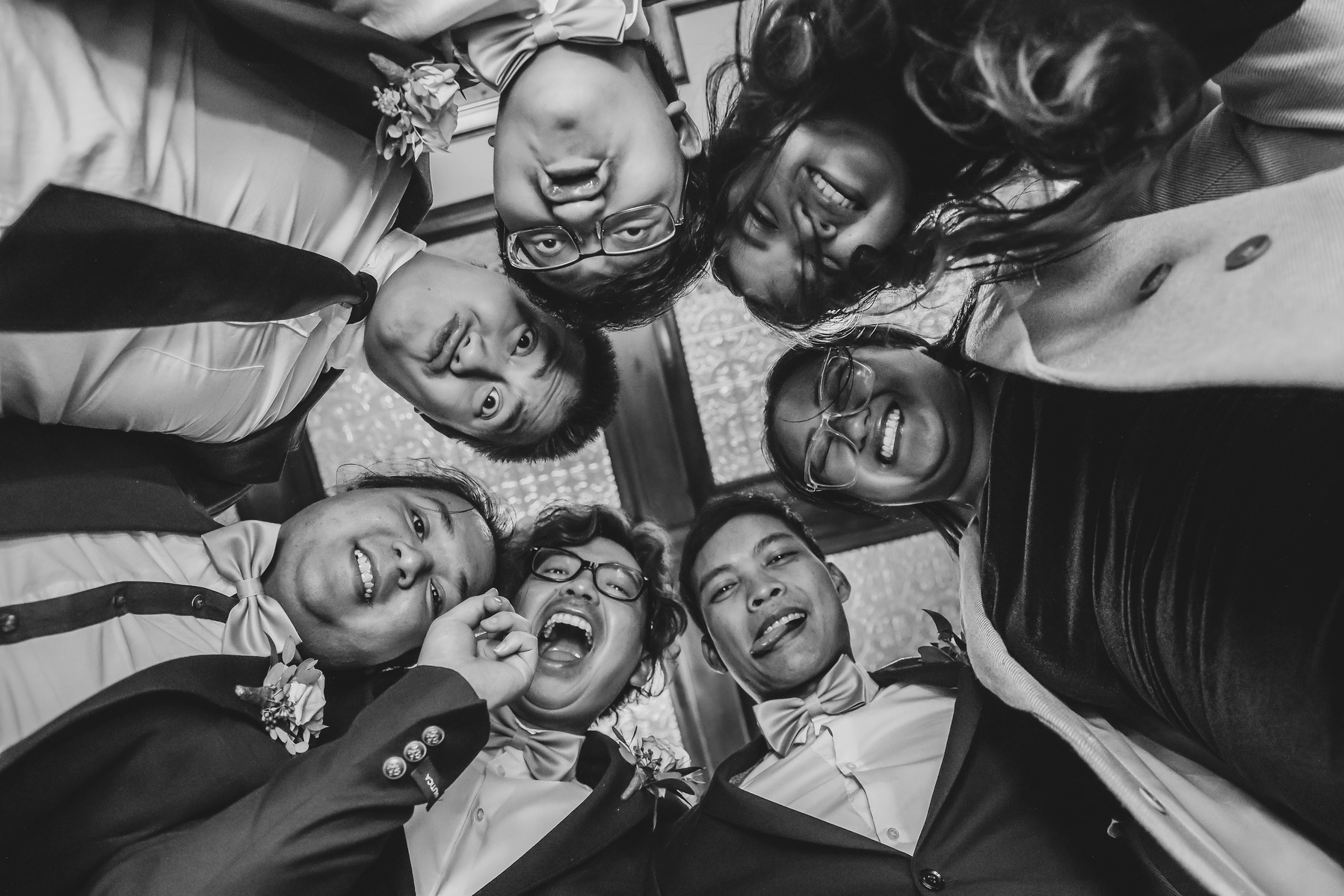black and white image of group of friends huddled together at a wedding, shot from below