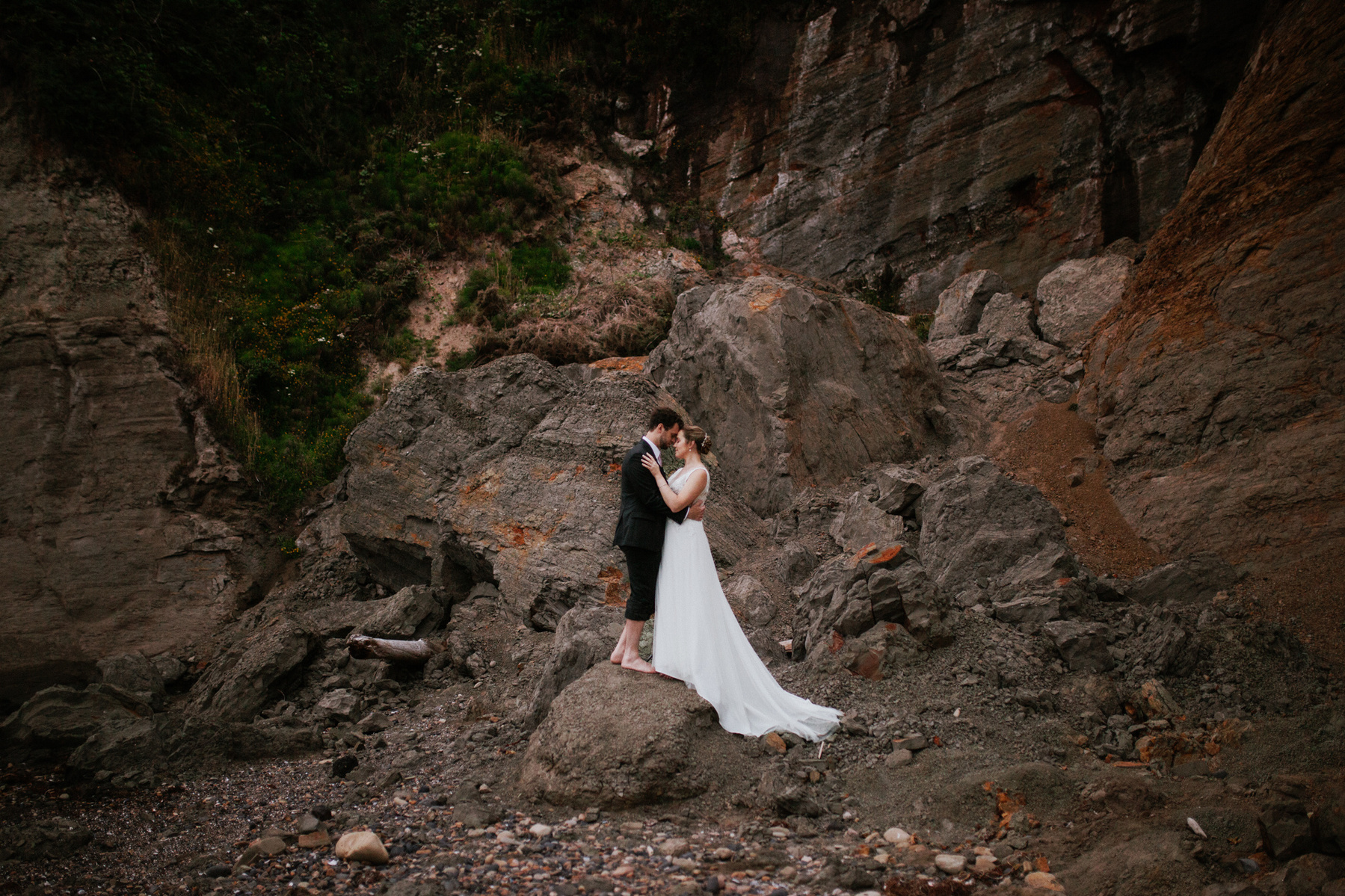 A newly married couple embracing on  a dark, rocky hillside on the Oregon Coast.