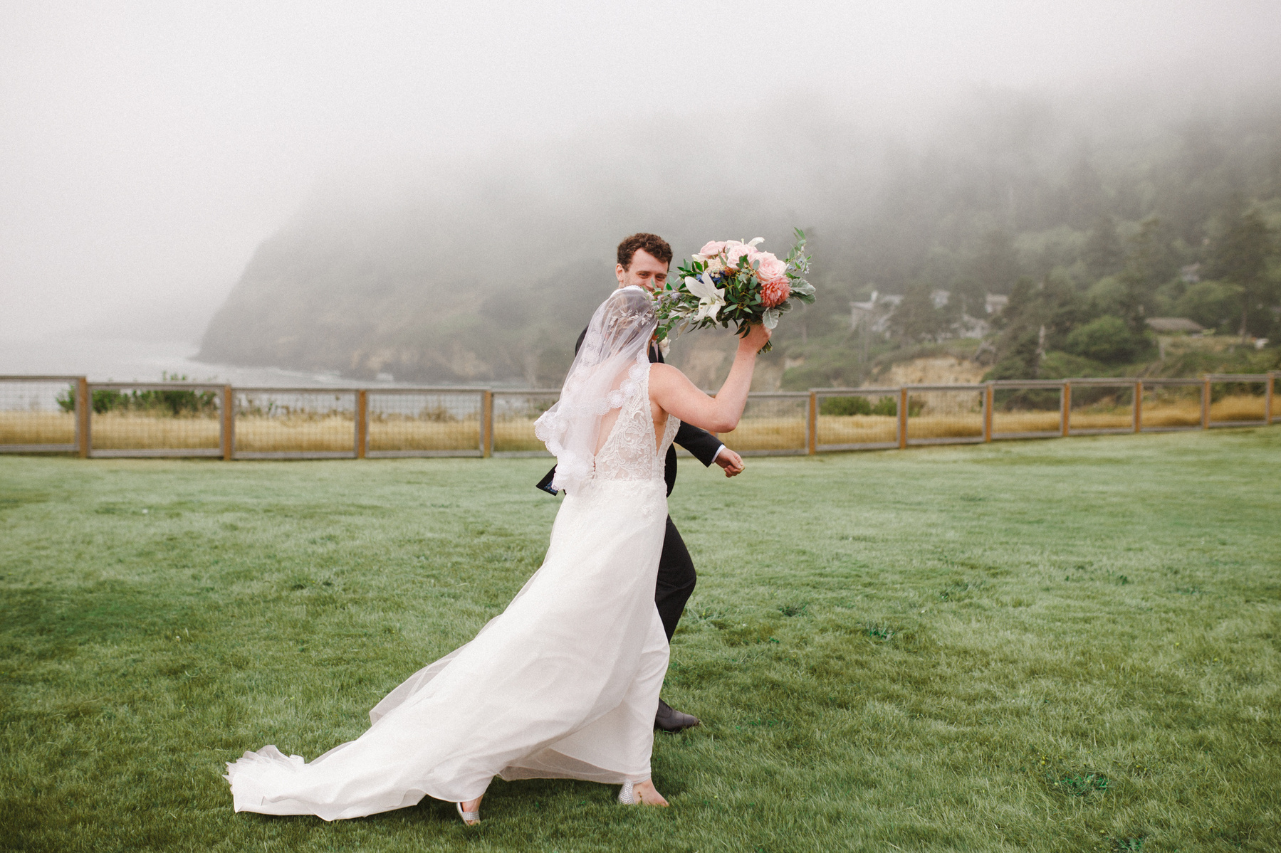 Bride and groom walking post-ceremony in front of a foggy, moody landscape on the Oregon Coast.
