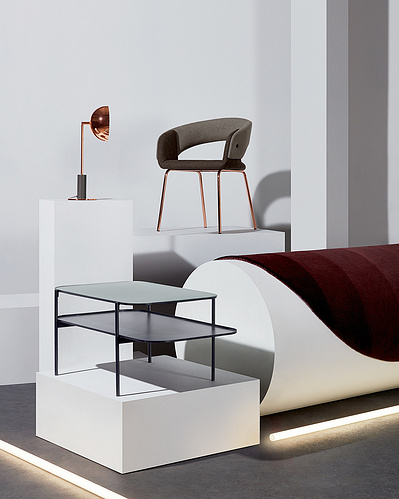 An elegantly composed image capturing the interior of a white room with a red sofa placed on a solid white object. This refined photograph is expertly crafted by David Lineton, a specialist in commercial still life photography in London.