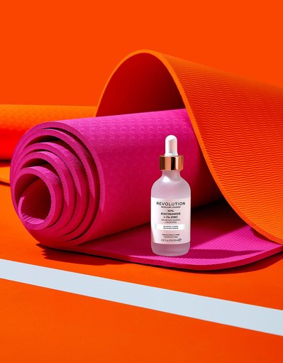 A chic presentation of cosmetic product placed on a rolled pink sheet, with an elegant orange sheet serving as the background. This stylish composition is skillfully photographed by David Lineton, an expert in London makeup still-life photography.