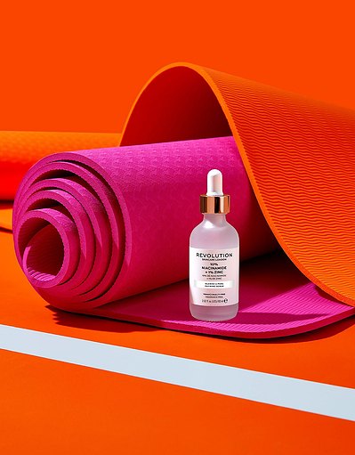 A chic presentation of cosmetic product placed on a rolled pink sheet, with an elegant orange sheet serving as the background. This stylish composition is skillfully photographed by David Lineton, an expert in London makeup still-life photography.