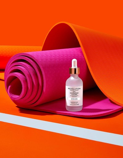 A chic presentation of cosmetic product placed on a rolled pink sheet, with an elegant orange sheet serving as the background. This stylish composition is skillfully photographed by David Lineton, an expert in London makeup still-life photography.