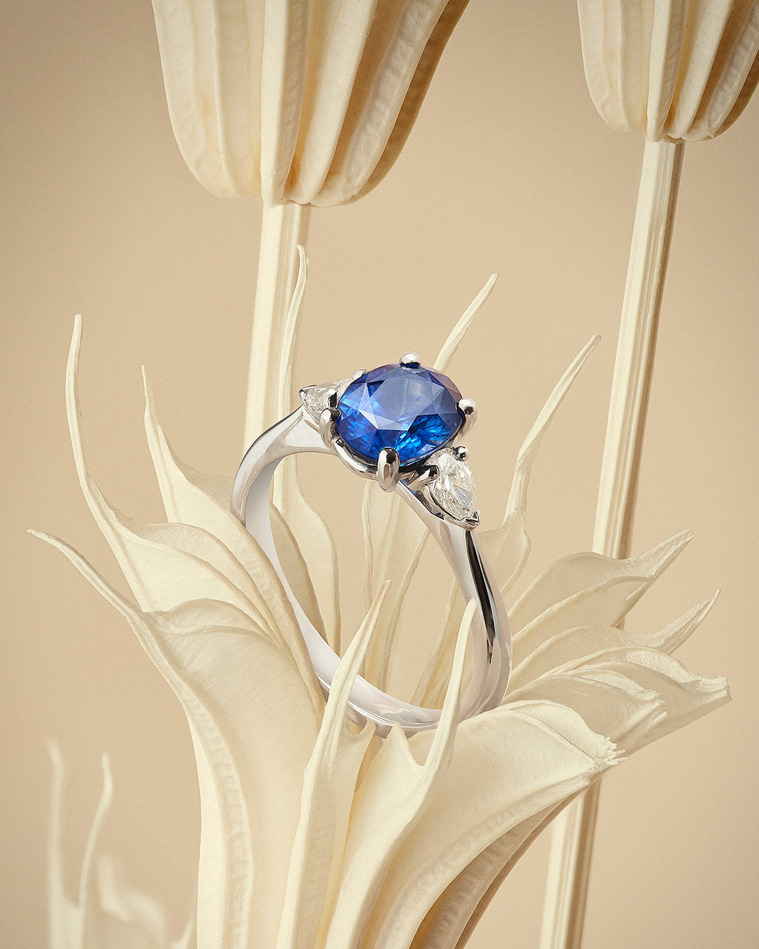 Dried flowers in a peachy nude tone, sits a brilliant blue sapphire gemstone with a diamond setting and Platinum mount. 