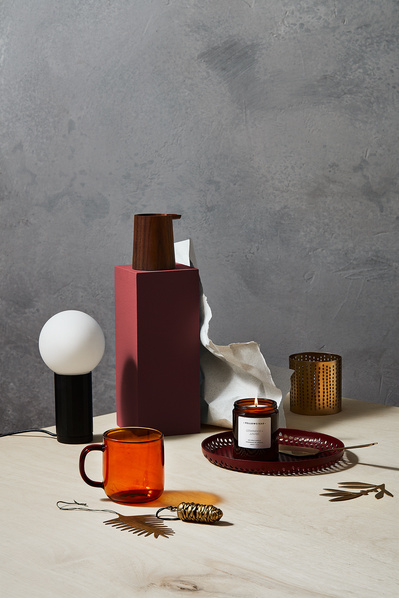 A captivating composition featuring a cup with a candle placed in a bottle, softly illuminated by an off lamp, accompanied by other products. Skillfully captured by David Lineton, an expert in product photography in London