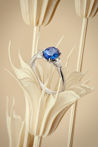 A captivating composition showcasing a ring with a blue stone elegantly placed on a flower sculpture. This visually appealing scene is skillfully photographed by David Lineton, an expert in jewelry photography services in London.