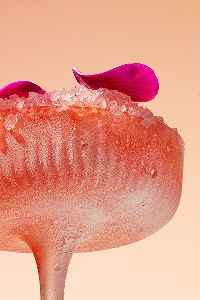 A refreshing image capturing a drink glass filled with small pieces of ice, adorned with two delicate flower leaves. This visually appealing composition is skillfully photographed by David Lineton, an expert in commercial drinks photography in London.
