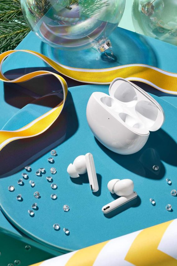 Music headphones and wireless earbuds sit on a brilliant oyster-blue surface with crystals scatted around the image. A yellow ribbon frames the headphones elegantly. 