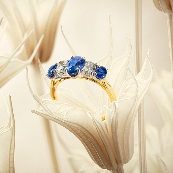 Engagement rings and three diamond and three oval sapphire setting with Yellow gold band sit in a peachy dried flower 