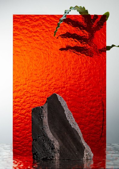 A striking composition capturing a scene of full reddish water with a large dark rock immersed in it, complemented by a sizable leaf placed in the water. This visually compelling image is skillfully captured by David Lineton, an expert in amazing still li
