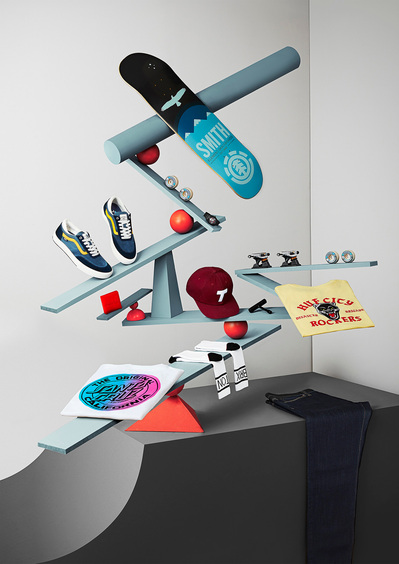 A creatively composed scene featuring a pair of shoes, socks, stacking board, cap, and various other products expertly balanced on a zigzag rod-type surface. Sikllfully captured by David Lineton, a distinguished creative product photographer in London.