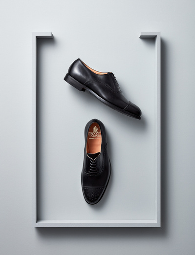 A minimalist and stylish composition featuring a pair of black shoes elegantly placed on a silver surface covered across three sides. Skillfully executed by David Lineton, an expert in product photography in London
